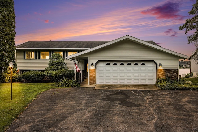 view of front of home with a garage, brick siding, driveway, and a yard