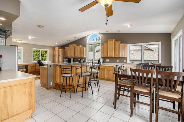 kitchen with light tile patterned floors, a breakfast bar, a ceiling fan, freestanding refrigerator, and lofted ceiling