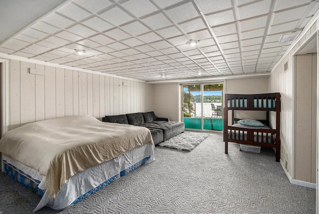 bedroom with wooden walls, carpet, visible vents, and access to exterior
