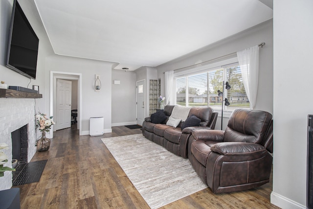 living room with baseboards, a brick fireplace, and dark wood finished floors