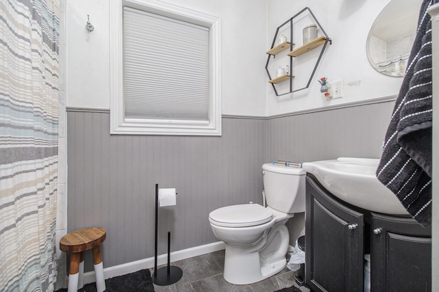 full bathroom featuring vanity, baseboards, a wainscoted wall, and toilet