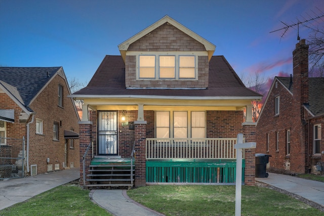 bungalow-style house featuring covered porch, a lawn, and a shingled roof
