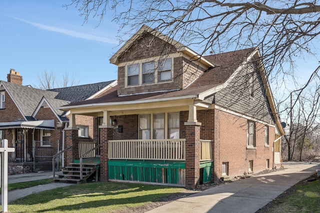 view of front facade with a porch, brick siding, roof with shingles, and a front lawn