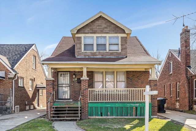 bungalow with a porch, brick siding, and roof with shingles