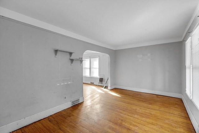 empty room featuring arched walkways, baseboards, plenty of natural light, and light wood-style floors