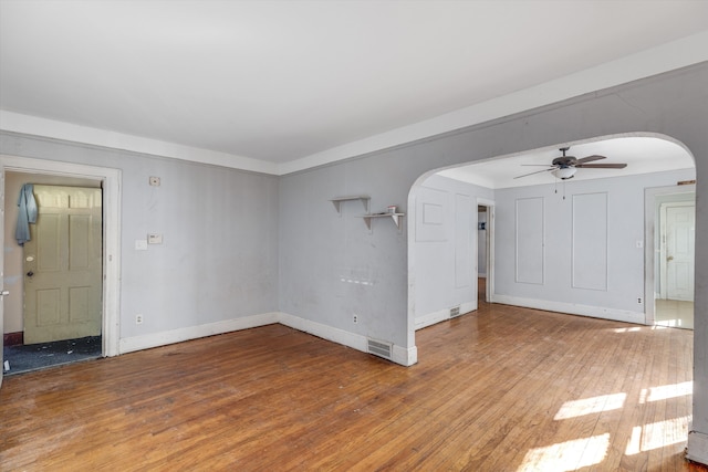 unfurnished living room featuring baseboards, arched walkways, a ceiling fan, and hardwood / wood-style floors