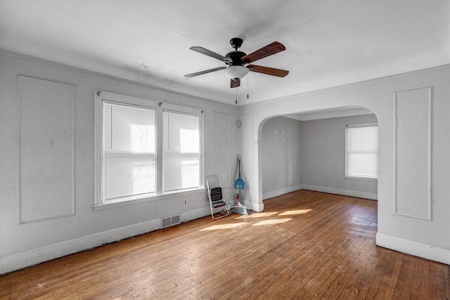 empty room featuring ceiling fan, visible vents, arched walkways, hardwood / wood-style flooring, and baseboards