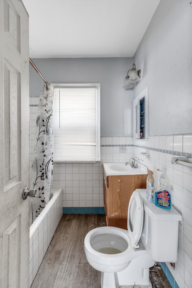 full bathroom featuring tile walls, wood finished floors, a wainscoted wall, toilet, and tiled shower / bath combo