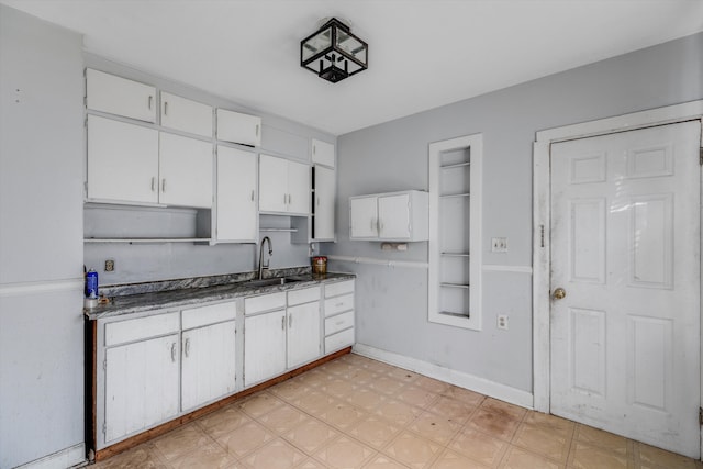 kitchen with dark countertops, a sink, baseboards, white cabinets, and light floors
