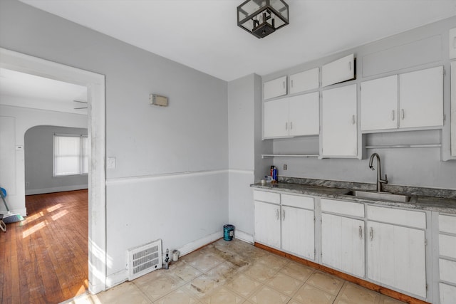 kitchen with visible vents, arched walkways, a sink, baseboards, and white cabinets