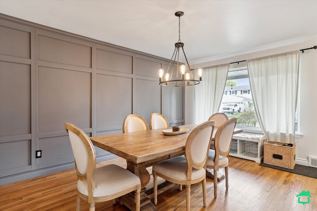 dining room featuring crown molding, visible vents, light wood-type flooring, a decorative wall, and a notable chandelier