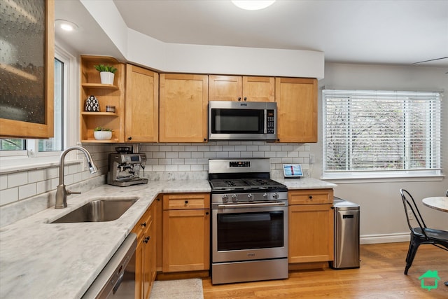 kitchen with light stone countertops, decorative backsplash, appliances with stainless steel finishes, a sink, and light wood-type flooring