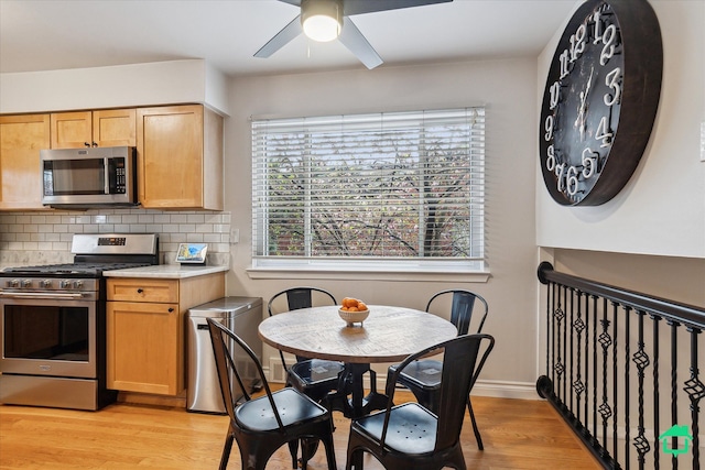 kitchen featuring appliances with stainless steel finishes, light countertops, light wood finished floors, a ceiling fan, and backsplash