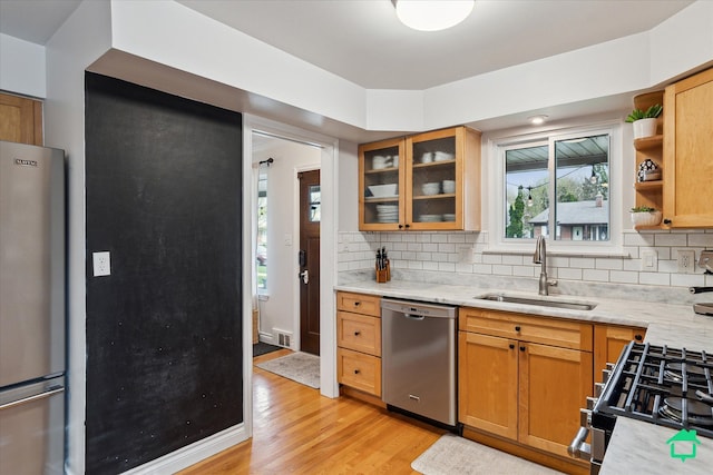 kitchen featuring stainless steel appliances, decorative backsplash, light wood-style flooring, and a sink
