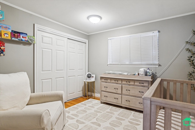 bedroom with crown molding, a crib, a closet, and light wood-style flooring