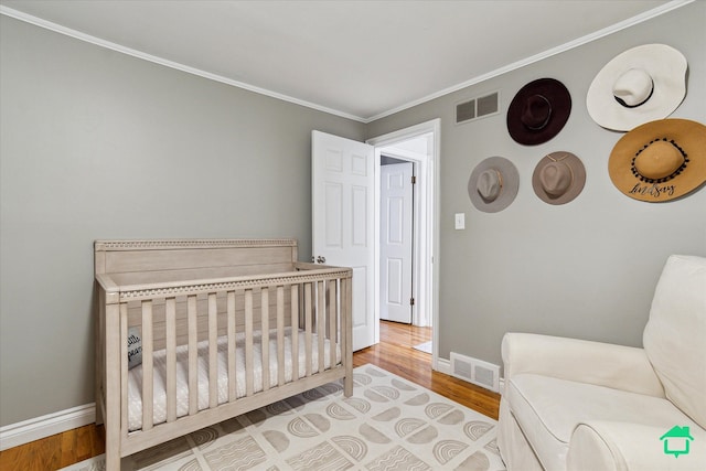 bedroom featuring wood finished floors, visible vents, crown molding, and baseboards