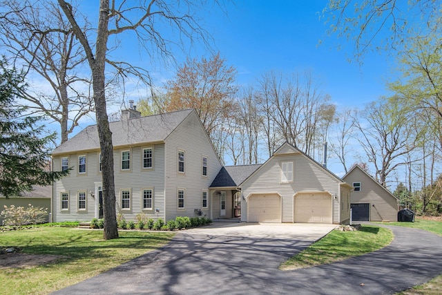colonial home featuring roof with shingles, a chimney, driveway, and a front lawn