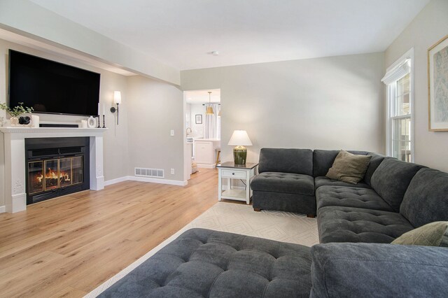living room featuring baseboards, visible vents, a glass covered fireplace, and light wood-type flooring