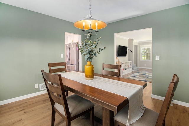 dining room featuring baseboards, visible vents, light wood-style flooring, and an inviting chandelier