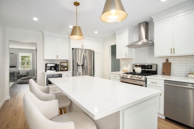 kitchen with a kitchen island, appliances with stainless steel finishes, tasteful backsplash, wall chimney exhaust hood, and light wood-style flooring