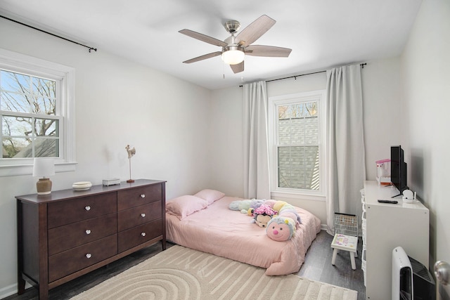 bedroom featuring baseboards, a ceiling fan, wood finished floors, and multiple windows