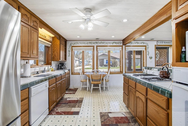 kitchen featuring a sink, tile counters, ceiling fan, light floors, and white appliances