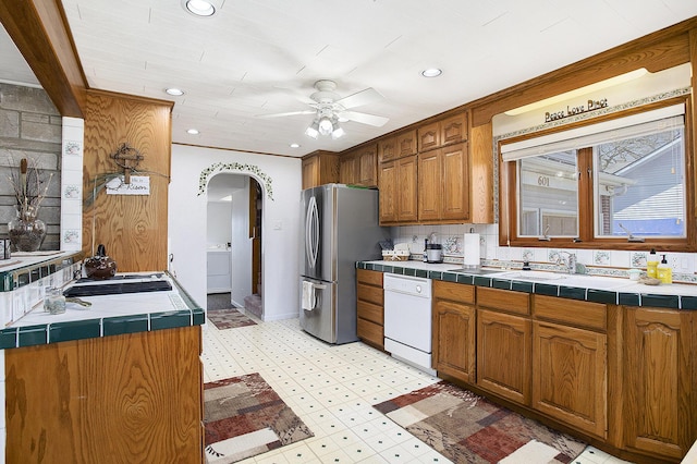 kitchen featuring light floors, freestanding refrigerator, tile counters, ceiling fan, and dishwasher