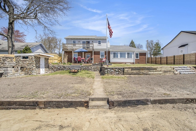 view of front of property featuring brick siding, fence, and a balcony