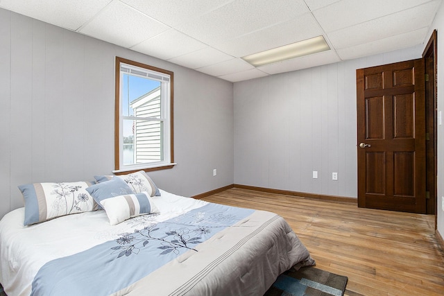 bedroom featuring a paneled ceiling, baseboards, wood walls, and light wood-style floors