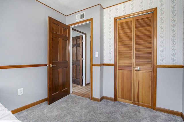 unfurnished bedroom with a closet, carpet flooring, baseboards, visible vents, and crown molding