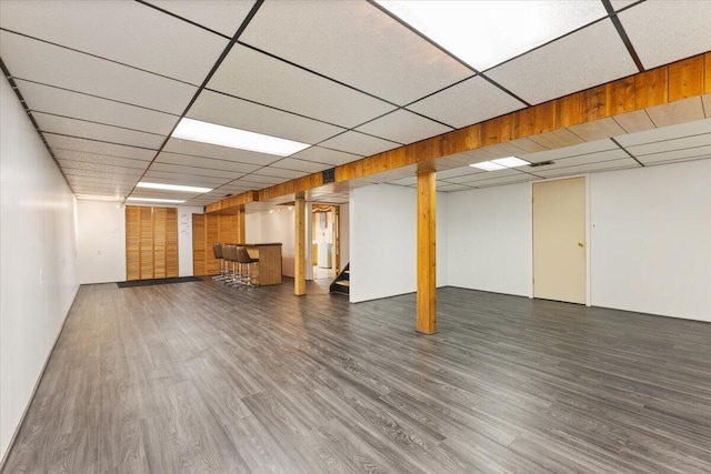 finished below grade area with bar area, wood finished floors, stairs, and a drop ceiling