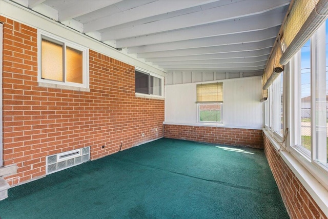 unfurnished sunroom featuring carpet, a healthy amount of sunlight, brick wall, and beamed ceiling