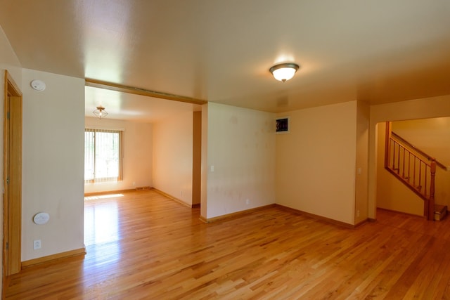 empty room featuring baseboards, visible vents, stairway, and light wood-type flooring