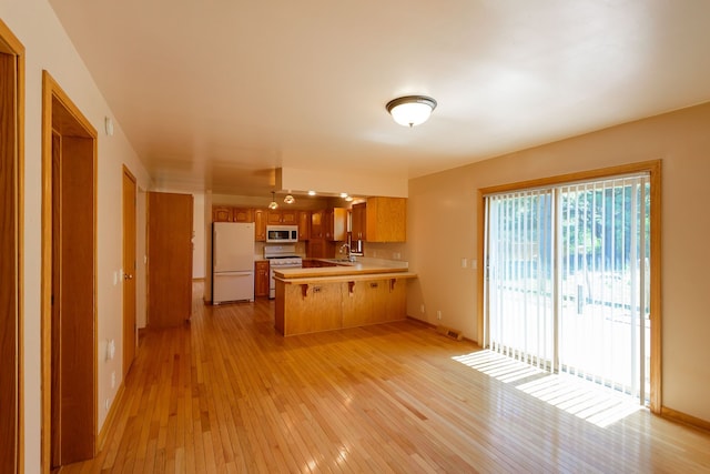 kitchen featuring light countertops, a sink, a peninsula, light wood finished floors, and white appliances