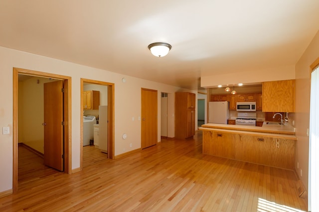 kitchen featuring a peninsula, white appliances, brown cabinets, a sink, and light wood finished floors
