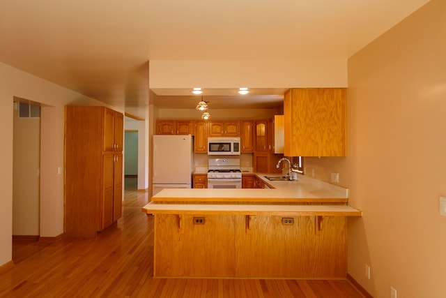 kitchen with white appliances, a peninsula, a sink, and light wood-style flooring
