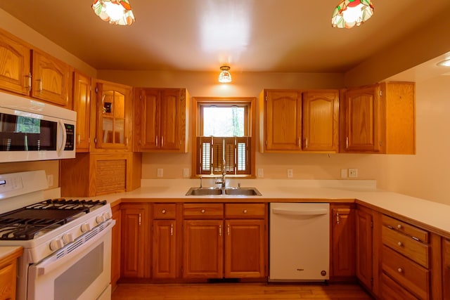 kitchen with a sink, light countertops, white appliances, and light wood-style flooring