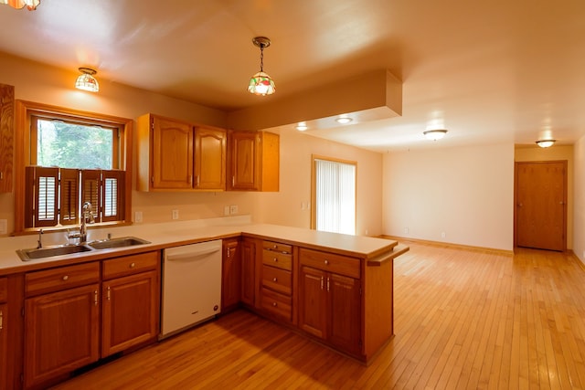 kitchen featuring white dishwasher, light countertops, a sink, light wood finished floors, and a peninsula
