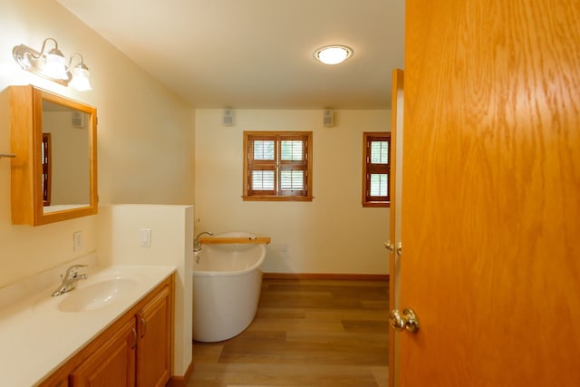 full bathroom featuring wood finished floors, baseboards, a soaking tub, and vanity