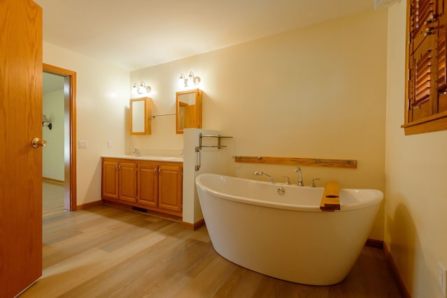bathroom with baseboards, a freestanding bath, wood finished floors, and vanity
