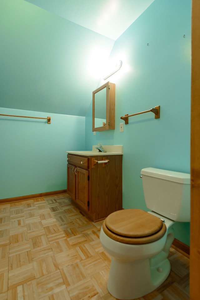 bathroom with toilet, baseboards, lofted ceiling, and vanity