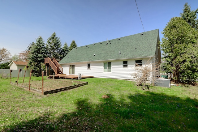 rear view of house featuring a lawn, a deck, fence, a shingled roof, and stairs