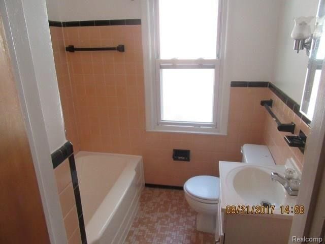 full bathroom featuring toilet, tile walls, and plenty of natural light