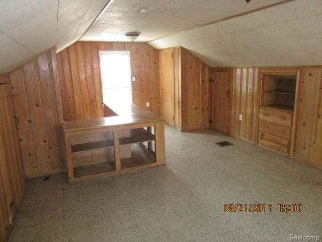 bonus room with lofted ceiling, wooden walls, and visible vents