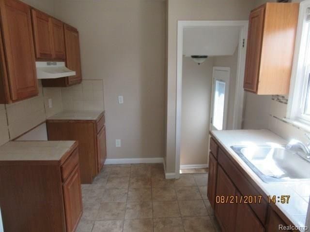kitchen with brown cabinetry, under cabinet range hood, light countertops, and a sink
