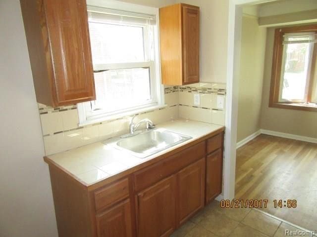 kitchen featuring brown cabinets, a sink, backsplash, and baseboards