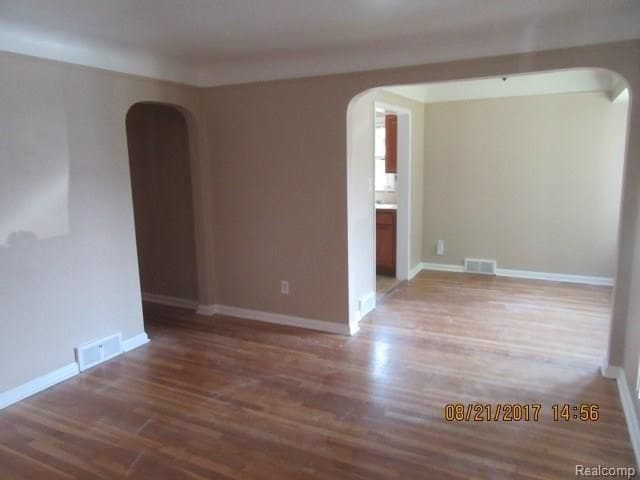 empty room featuring visible vents, arched walkways, and wood finished floors