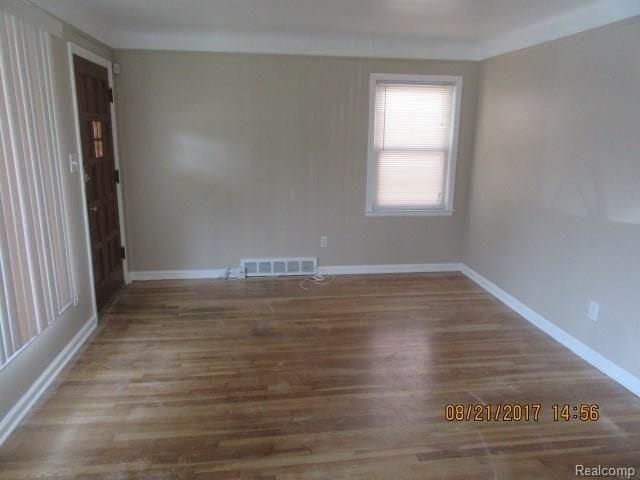 unfurnished room featuring wood finished floors, visible vents, and baseboards