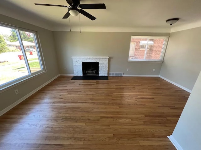 unfurnished living room with visible vents, a brick fireplace, wood finished floors, baseboards, and a ceiling fan