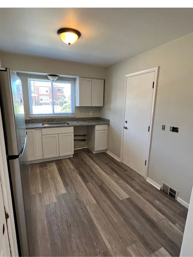 kitchen featuring dark wood-type flooring, freestanding refrigerator, built in desk, and dark countertops